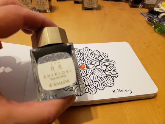 Hand drawn generative/procedural art in ink on an open page of my sketchbook. The abstract pattern is floral. I'm holding a small bottle of ink in front of my sketchbook.