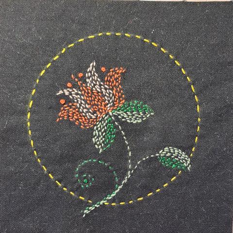 Auf ein schwarzes Quadrat Baumwollstoff wurde eine stilisierze Lotusblüte im Kanthastil gestickt.