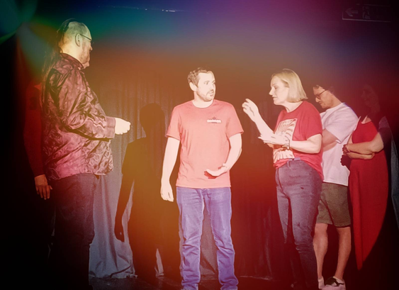 More performers,  standing around on a stage talking.