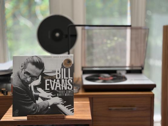 Bill Evans - Momentum LP cover.

A full-bleed black and white photo of Evans at the piano, looking back over his shoulder. Title and artists to the right.

The black LP plays on a vintage, restored Bang & Olufsen Beogram 4000 linear-tracking turntable to the right.