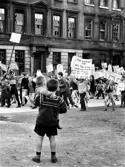 A black-and-white photo of a protest of children walking through Glasgow streets carrying protest signs and banners. One is particularly visible, and reads:

'THE VENNY FOR
EVER
DONT PUL IT DOWN
WERE WILL WE GO TO
IF YOU PULL IT DOWN
THERE IS NO
PLACE ELSE'

In the foreground a child holds their sibling as they watch the march.

Photo: https://www.glasgowtimes.co.uk/news/19203889.never-mess-glasgow-wean---gorbals-kids-revolted-threat-playground/