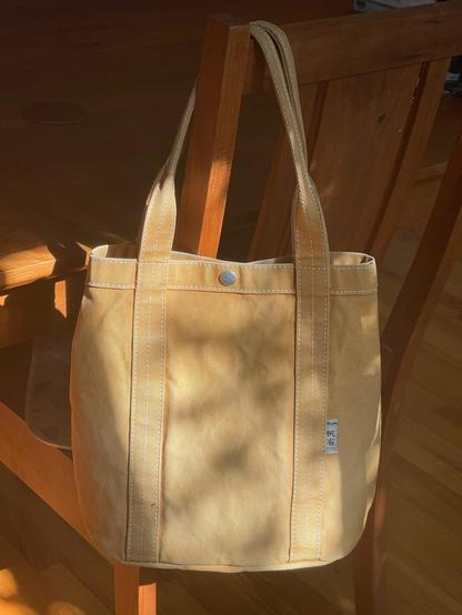 It's a really lovely canvas tote in camel hanging on the back of a chair.