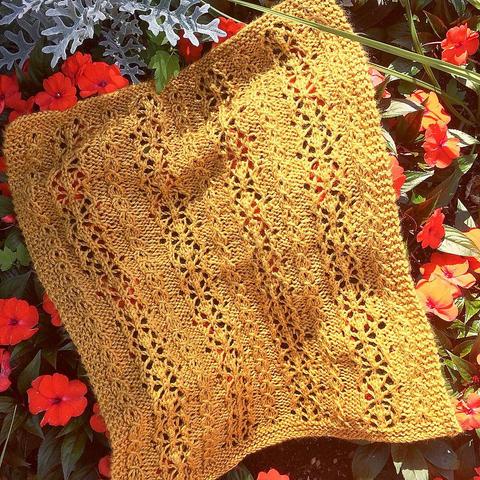 photo of a small golden colored doll-sized lacy blanket laid over a patch of red-orange flowers.