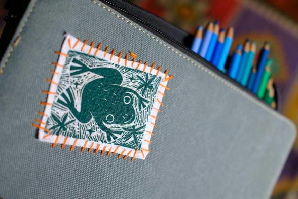 a canvas pencil case with a hand printed frog linocut patch sewed into the cover with an orange thread. Pencils are visible sticking out from the case.