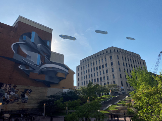 Color image of three Goodyear airships soaring over Downtown Akron, Summit County, Ohio, USA, June 3, 2025. Image shows three modern-era Goodyear airships  flying together over Lock 2 Park and the AT&T art deco building celebrating 100 years of commercial airship dominance during Akron Mayor Shammas Malik's 2025 State of the City Address.