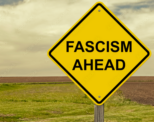 A yellow warning sign on a pole, with a field, dirt road, and cloudy sky in the background. The words on the sign read: "FASCISM AHEAD"