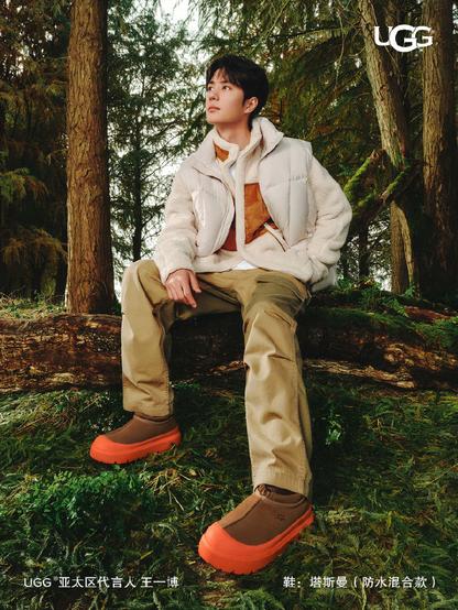 Ad image featuring Wang Yibo modelling Ugg clothes and shoes, sitting on a log in a forest.