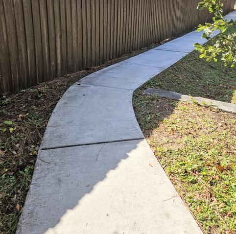 Bright white pedestrian sidewalk bends and curves to follow the edge of a wooden property fence.