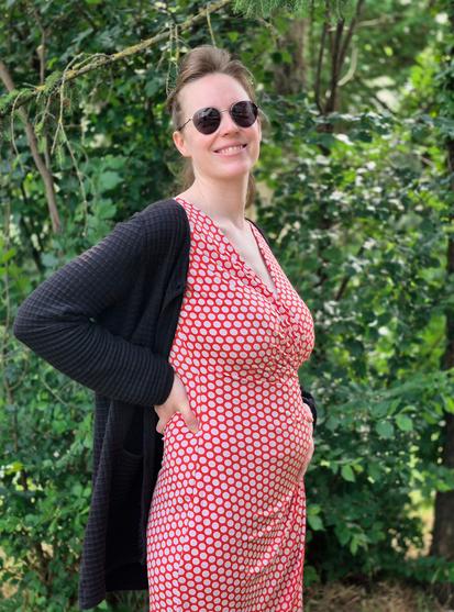 Il s’agit d’une photo de moi en extérieur, où je porte une robe rouge à pois blanc. Je souris et montre fièrement mon ventre de femme enceinte. Je rentre tout juste dans mon 2e trimestre, il n’est donc pas très imposant pour l’instant, mais j’en suis très contente.