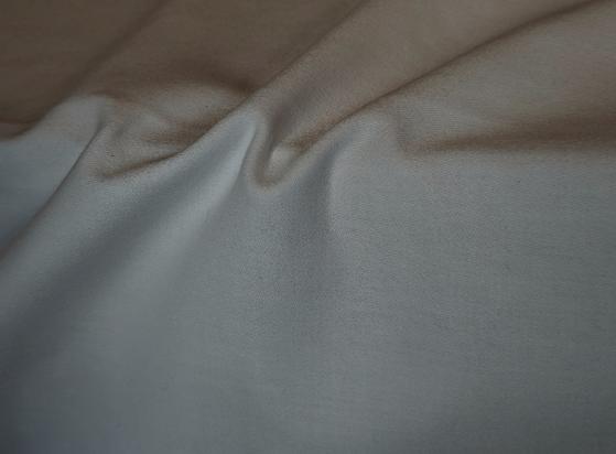 Close-up of wrinkled fabric in neutral tones, showing soft folds and creases in an off-white table cloth with a fine weave texture creating gentle shadows and highlights across the surface.