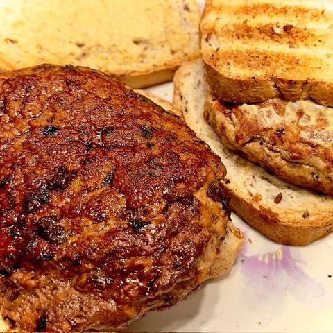 Two thick turkey hamburgers are shown sitting on toasted bread upon which mustard has been spread. The burger on the left is covered with pan deglazing that makes it look caramelized and especially delicious. The burger on the right does not show any deglazing, but looks tasty nonetheless. Both burgers were fabulous and fluffy.