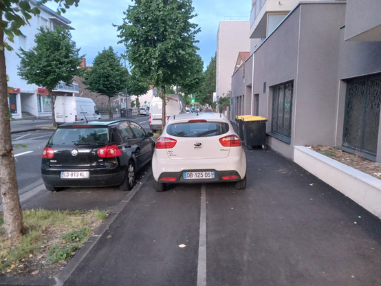 KIA blanche DB-125-DS garée comme une merde à cheval sur le trottoir et sur la piste cyclable.