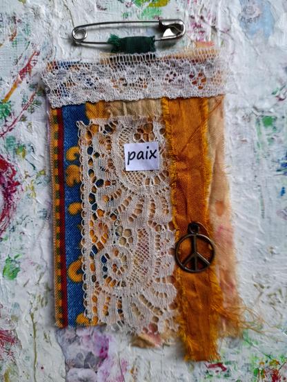 Fabric rests in orange and blue nuances, vintage lace, a copper peace sign and the word paix = peace.