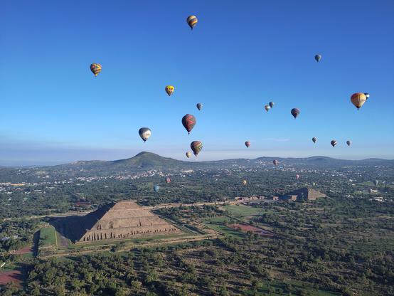 Foto. Pyramiden aus der Vogelperspektive, mit Heissluftballonen am Himmel.