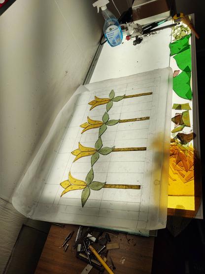 Four little daffodils, laying on tracing paper on a light table. They're made from green and yellow glass, and waiting for a background to be added.