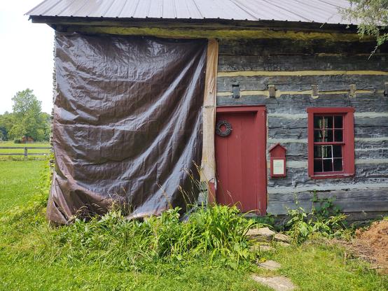 A two hundred year  old log cabin with a tarp draped over one end , hiding some severely scary structural issues.