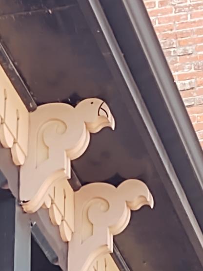 A corbel on the side of a porch, cream white against black, with the bird head outlined in black.