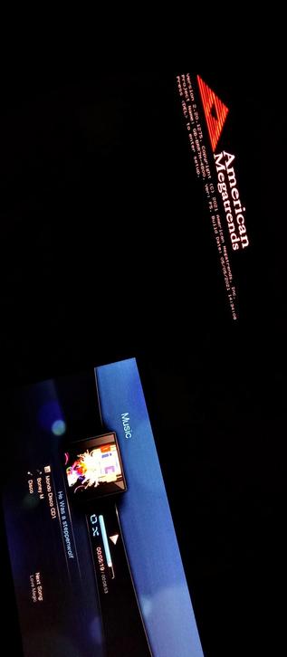 The composition shows a screen with a dark background and a red logo in the top right corner that reads "American Megatrends" with a version number "2.20 - 1275" and a copyright notice. Below the logo, there is text indicating the project name, version, and build date. 
The Mini PC is stuck here. Crashed and in a loop 
The other IPS LED panel also displays a music player interface with a track titled "He Was a Steppenwolf" by Mondo M, with a progress bar showing the current time as 00:51 out of 00:53. The next song listed is "Love Magic." The word "Music" is visible on a blue bar at the bottom of the screen. The overall layout suggests a computer or media player interface.

 Ovis2-8B

🌱 Energy used: 0.192 Wh