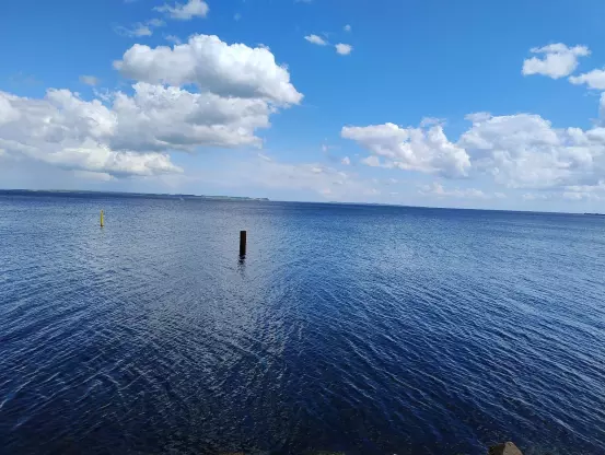 Blick auf ein blaues Meer, blauen Himmel und einige weiße Wattewolken.

Ziemlich genau in der Mitte ragt ein Holzpflock aus dem Meer