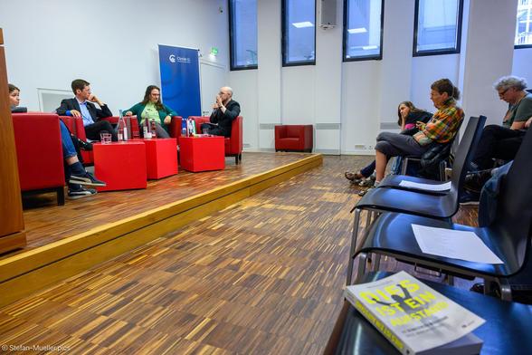 Podiumsiskussion zur Klimakrise mit Samira Ghandour, Fridays for Future, Prof. Dr. Mark Lawrence, Forschungsinstitut für Nachhaltigkeit Potsdam, Dr. Judith Enders, Uni Leipzig, und Dr. Fabian Telschow als Moderator. Im Vordergrund liegt ein Buch mit dem Titel „Dies ist ein Aufstand“. Mit kariertem Hemd der Biologe Michael Winter, der beinahe beim Hungerstreik verhungert wäre und Judith Beadle von der ehemals Letzten Generation jetzt Neuen Generation, Grimm-Zentrum, Humboldt-Universität zu Berlin, 05.06.2025