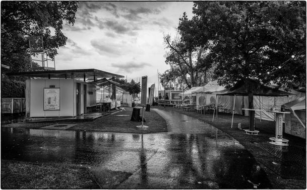 Schwarzweissfotografie eines menschenleeren Festgeländes im Regen.