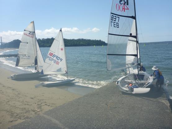 Sailing dinghies launching at Ambleside Beach. One boat is on the ramp and two boats are sitting on the beach. Boats are: RS Vision, Laser, and RS 400.