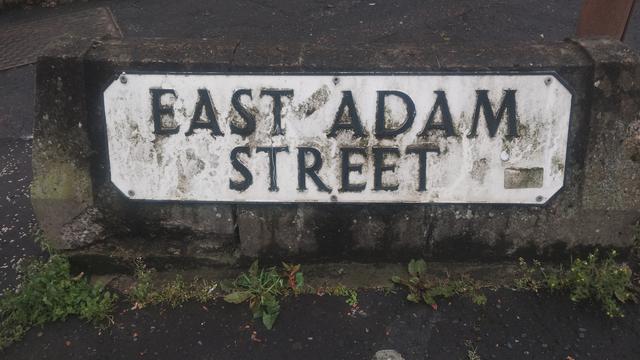 A rather muddy street sign, for East Adam Street
