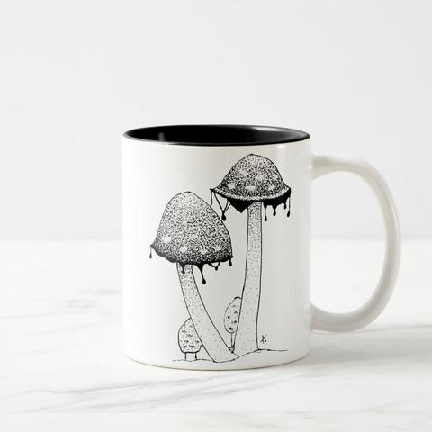 product image of a mug on the sides are a pen an dink stippled drawing of two slightly melt  inky cap mushrooms. The inside and rim of the mug have been glazed in black to match the drawing.