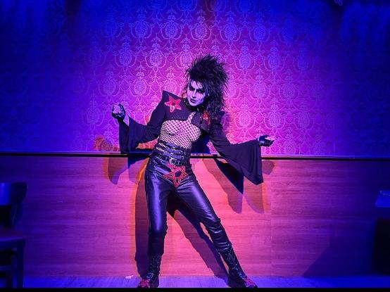 Person in a goth outfit with Kiss make up and a black wig on stage.