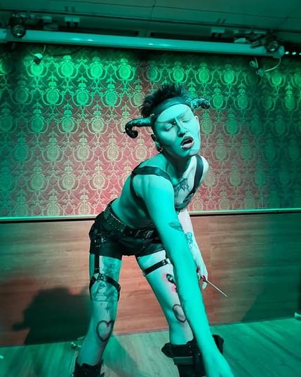 Person with devil horns wearing a leather strips on stage. Leaning forward.