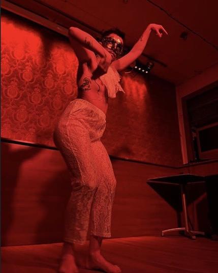 Person dancing with both arms in the air wearing a mask on stage.