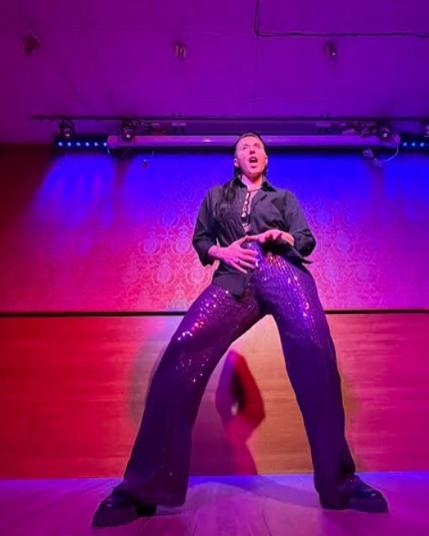 Person with purple glitter pants and black shirt dancing on stage.