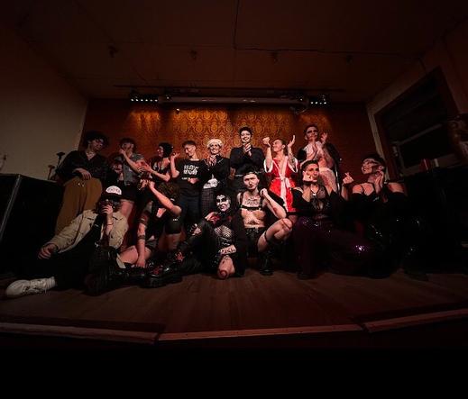 Group photo. Two rows of drag performers on stage.