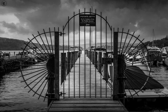 metal gate with semicircle sides covered in spikes leading onto a wooden jetty lined with small boats