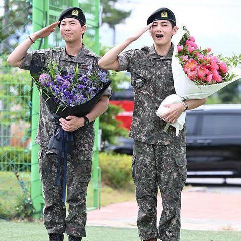 RM and V of BTS saluting while holding bouquets of flowers.