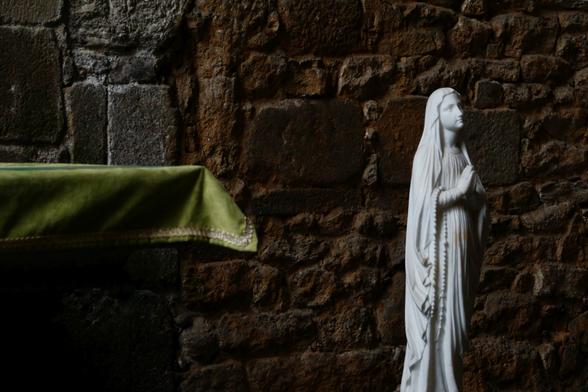 A white figure of a praying Mary on the right, green tablecloth on the left side, a stone wall in the background