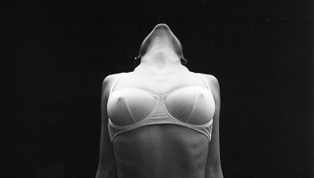 une femme en soutien-gorge se dresse, épaules et tête en arrière, menton levé