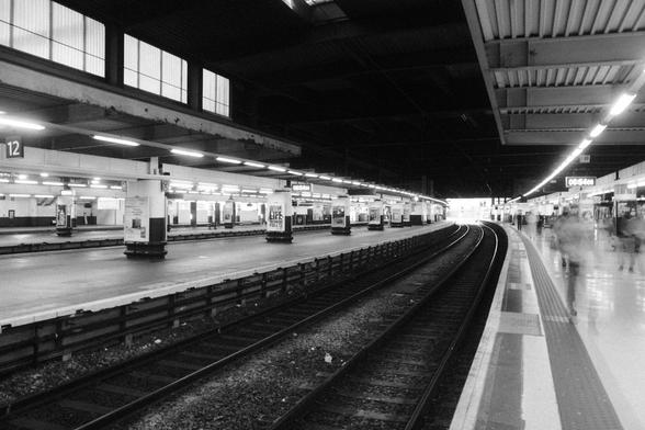Longer exposure photo of a train station with visible track and people walking down the platform.