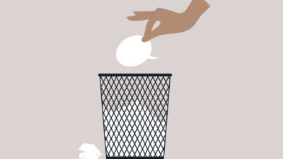 A hand dropping a speech bubble into a black trash can, symbolizing discarding unwanted ideas or messages.