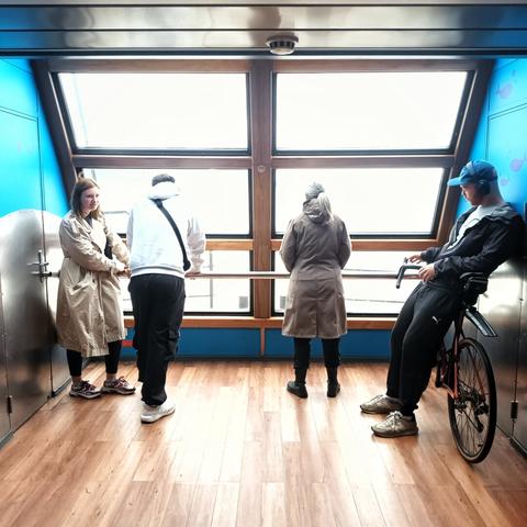 people in front of a very bright window, one of them stands besides a bike. the walls are blue, the ground is wooden. it is very symetrical.