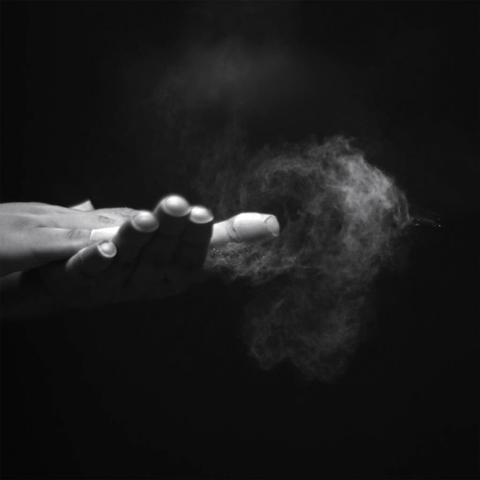 Black and white image of human hands clapping fingers-to-palm. Baby powder is jetted out from the hands, revealing the flow created.