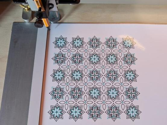 a two colour geometric tiled pattern sitting on the bed of a pen plotter