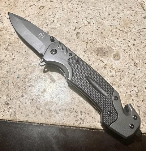 A folding knife with a stainless steel blade and a textured black handle, resting on a light-colored surface.