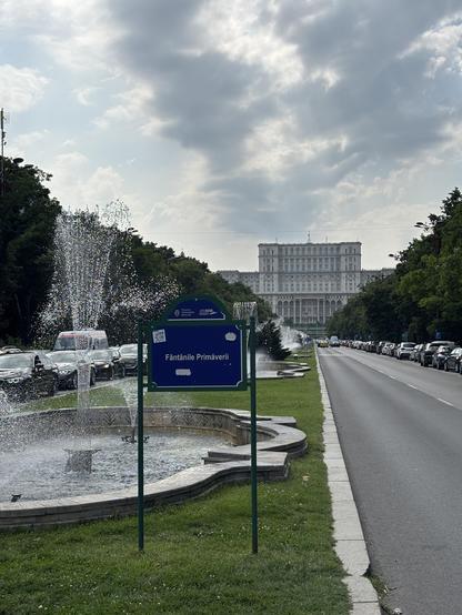 Vast concrete building in the distance, beyond a fountain.