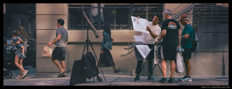 An artist stands next to an easel and stand of their works, showing several interested passerby a newspaper article, perhaps about themselves.