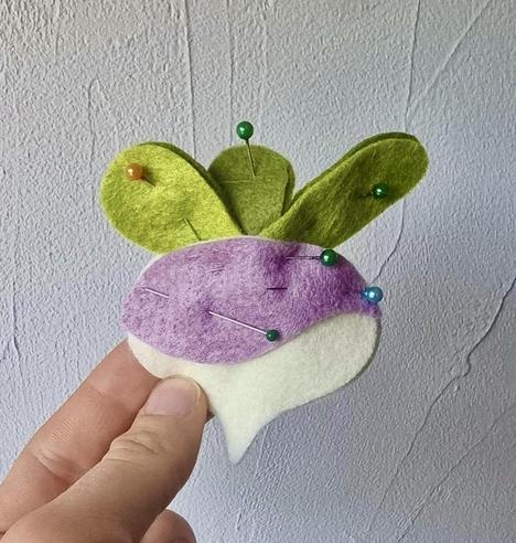 Picture of an unfinished felt turnip held in front of a white wall. The felt is not sewn on, but pinned together.