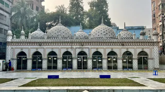 The image depicts a building with intricate architectural details, featuring multiple domes and arched windows. The structure appears to have a decorative facade, possibly made of tiles or covered with ornamental designs. Surrounding the building is a paved area with a landscaped lawn. The overall style suggests it may be a mosque or a cultural monument, likely located in a region with rich historical influences.

Image Credits: Wikimedia / Dead.rabbit / CC BY-SA 4.0