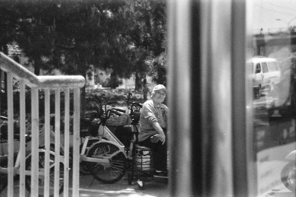 Ilford FP4 E.I. 64

English alt text: A black and white photograph of a person sitting on a bench next to a bicycle, with several bicycles parked nearby. Trees and a building are visible in the background.

Chinese alt text: 一张黑白照片，画面中一个人坐在长凳上，旁边有一辆自行车，附近停放着几辆自行车。背景中可以看到树木和一栋建筑。