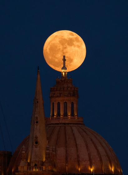 A full moon known as the Strawberry Moon rises behind the steeple of St Paul's Anglican Cathedral and the dome of the Basilica of Our Lady of Mount Carmel in Valletta