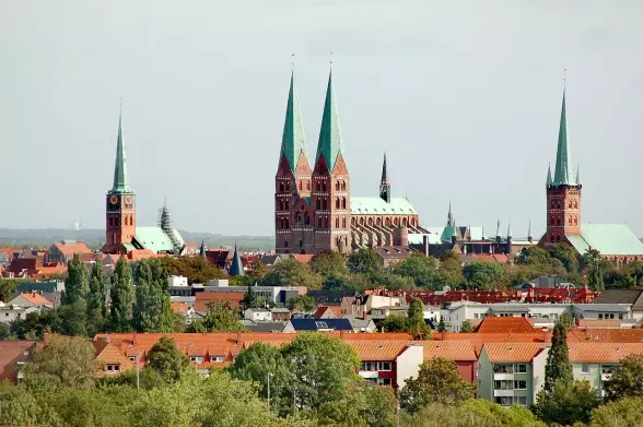 The image depicts a picturesque view of a city skyline featuring several notable buildings with distinctive spires and rooftops, including a large structure with multiple green-tipped towers. It appears to show a blend of urban architecture set against a backdrop of trees and lower buildings. The overall scene conveys a sense of historical significance and charm. If you need information about the specific buildings or location, feel free to ask!

Image Credits: Wikimedia / Oleg Dejan / CC BY 3.0